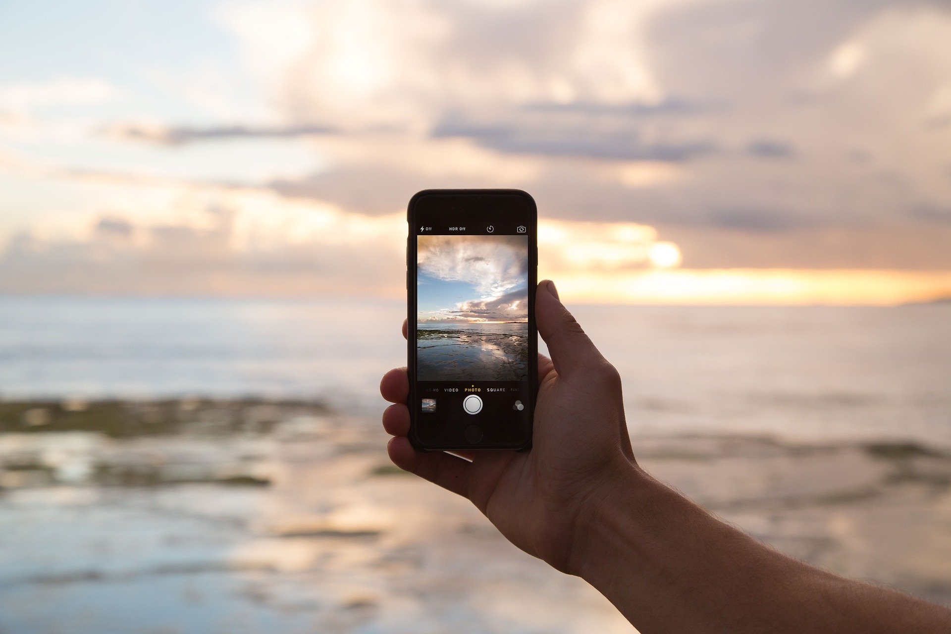 Image of someone taking a picture of sunrise over water using cell phone